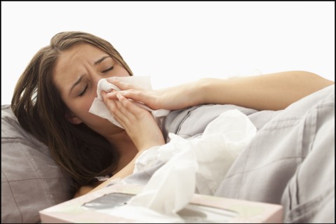 Young woman lying in bed blowing nose. Photo : Mike Kemp