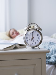 Woman in bed with alarm clock in foreground. Photo : Daniel Grill