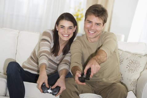 Couple sitting on sofa, playing video games.