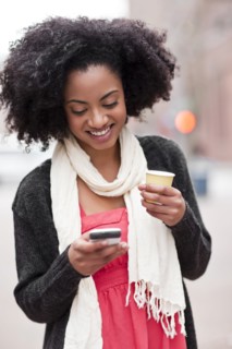 USA, Washington State, Seattle, Cheerful young woman text messaging while holding takeaway coffee.