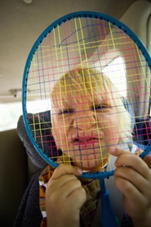 Portrait of boy (6-7) holding badminton racquet over face. Photo : Noah Clayton