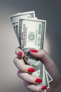 Close up of woman's hand with red nail polish holding bunch of dollar banknotes.