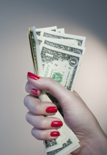 Close up of woman's hand with red nail polish holding bunch of dollar banknotes.
