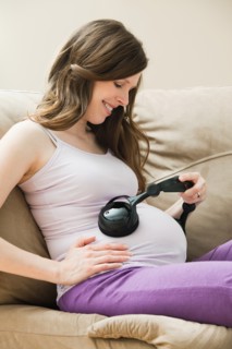 Young pregnant woman playing music through headphone to unborn baby. Photo : Mike Kemp