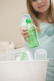 Studio shot of girl (8-9) holding plastic bottle above recycling bin. Photo : Mike Kemp