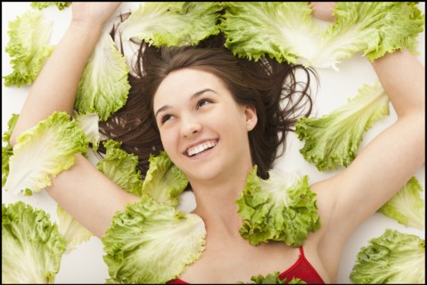 Young woman lying in lettuce leaves. Photo : Mike Kemp