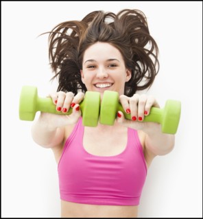 Studio portrait of young woman holding hand weights. Photo: Mike Kemp