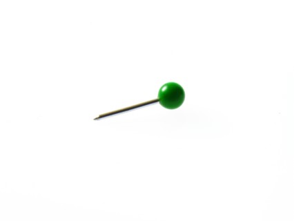 Green push pin on white background. Photo : David Arky