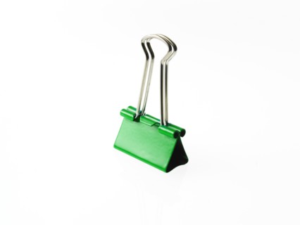 Green bulldog clip on white background. Photo : David Arky