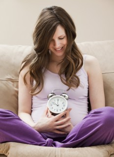 Young pregnant woman holding alarm clock. Photo: Mike Kemp