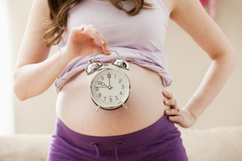 Young pregnant woman holding alarm clock. Photo: Mike Kemp