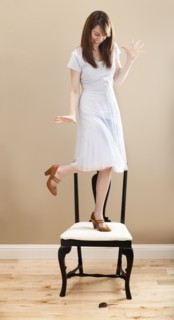Young woman standing on chair, evading mouse. Photo : Mike Kemp