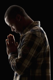 Studio shot of young man praying. Photo : Mike Kemp