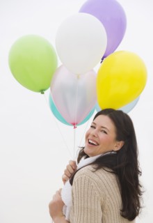 Young woman holding bunch of balloons laughing.