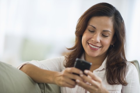 Smiling woman sitting texting on mobile phone.