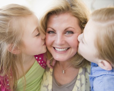 Daughters (8-11) kissing mother. Photo : Jamie Grill Photography