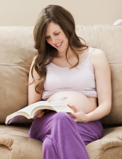Young pregnant woman sitting on sofa, reading book. Photo : Mike Kemp