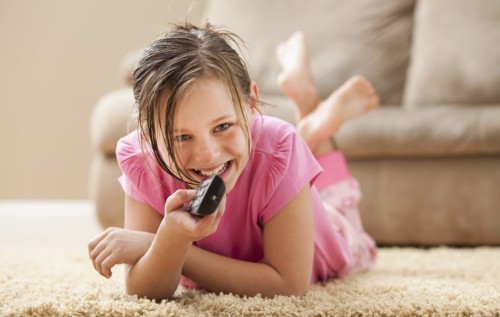 Portrait of girl (10-11) lying on floor holding remote control. Photo : Mike Kemp