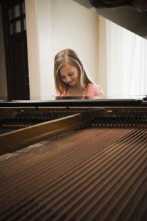 Girl (8-9) playing on grand piano. Photo : Mike Kemp