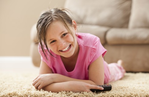Portrait of girl (10-11) lying on floor holding remote control. Photo : Mike Kemp