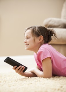 Girl (10-11) lying on floor holding remote control. Photo : Mike Kemp