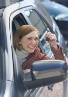 Woman sitting in new car showing car key.