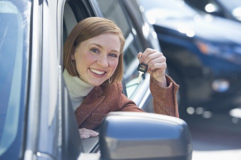Woman sitting in new car showing car key.
