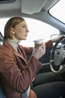 Woman driving car and drinking coffee.