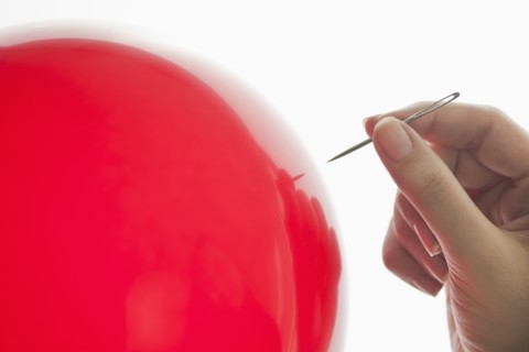 Studio shot of woman holding needle close to red balloon.