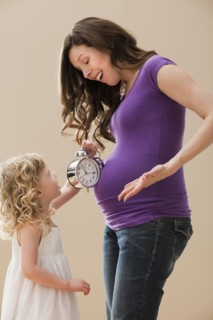 Girl (2-3) holding alarm clock next pregnant mother belly. Photo: Mike Kemp