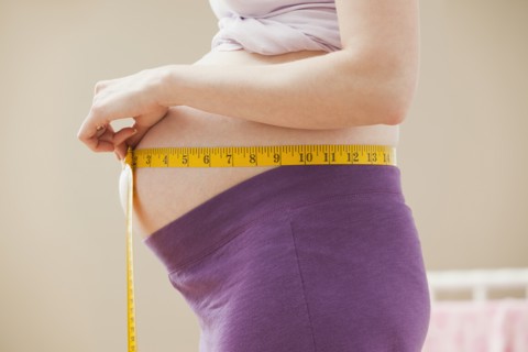 Young pregnant woman measuring belly. Photo : Mike Kemp