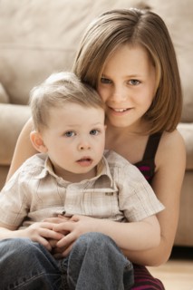 Portrait of Girl (10-11) with brother (2-3) sitting on floor. Photo: Mike Kemp