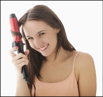 Studio portrait of young woman curling hair. Photo: Mike Kemp