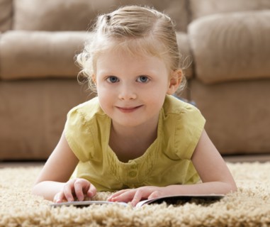 Portrait of smiling girl (2-3) lying on rug with book. Photo : Mike Kemp