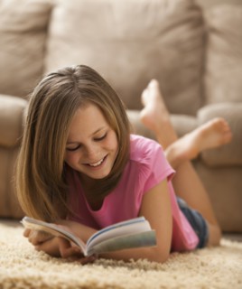 Girl (10-11) lying on rug, reading book. Photo : Mike Kemp