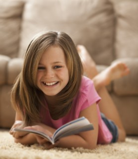 Portrait of girl (10-11) lying on rug with book. Photo : Mike Kemp