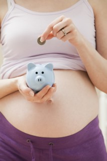 Young pregnant woman putting coin into blue piggybank. Photo: Mike Kemp