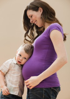 Portrait of boy (2-3) leaning pregnant mother's belly. Photo : Mike Kemp