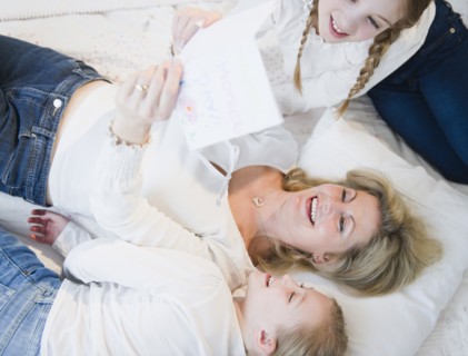 Mother and daughters (8-11) reading letter on bed. Photo : Jamie Grill Photography