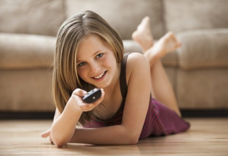 Girl (10-11) lying on floor, watching TV. Photo : Mike Kemp