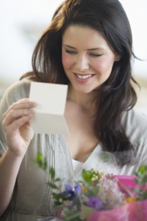 Young woman holding bouquet and reading greeting card.