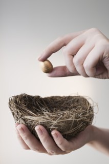 Studio shot of hand putting small gold egg into nest.