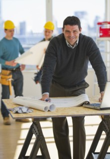 Architect preparing blueprintConstruction workers in background.