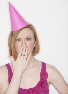 Woman wearing pink party hat covering lips with hand.