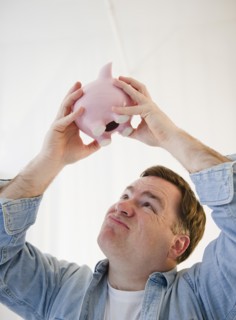 Man shaking piggy bank. Photo : Jamie Grill Photography