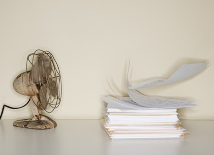 Electric fan blowing on heap of papers.