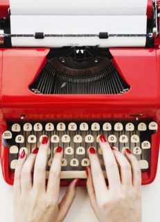 Close up of woman's hands with red nail polish typing on antique typewriter.