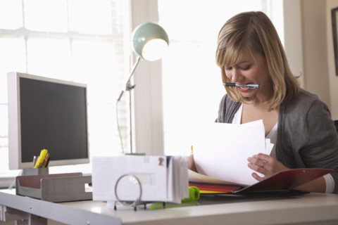 Woman working in office with pen in mouth. Photo : DreamPictures