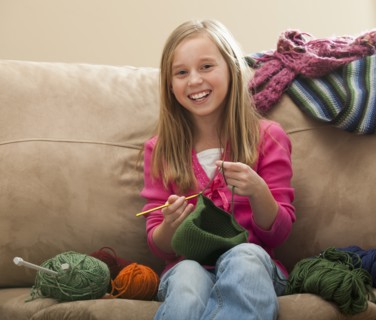 Cheerful girl (8-9) knitting woolly hat. Photo: Mike Kemp