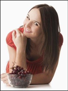 Studio portrait of young woman with grapes. Photo : Mike Kemp